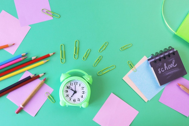 Stationery and alarm clock pencils pastel colored paper on a green background top view