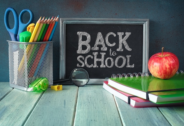 Stationery, apple and banana on a wooden table in front of blackboard with text