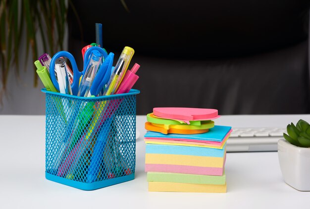 Stationery in a blue metal stand stand on a white table, workplace