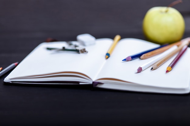 Stationery and a green apple are on the black table