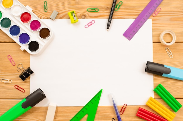 Stationery lie on a wooden table around a white sheet of paper