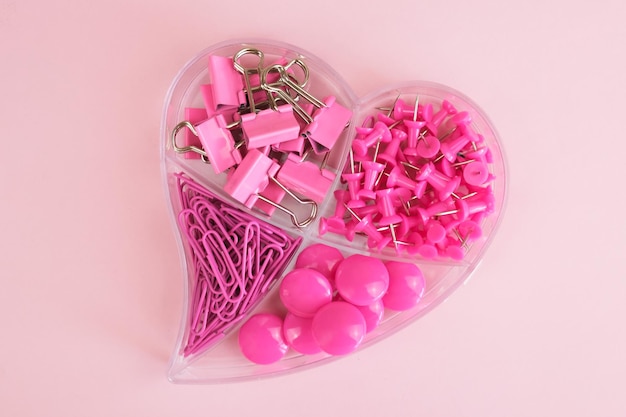 Stationery in pink color in a transparent plastic box in the shape of a heart on a pink background