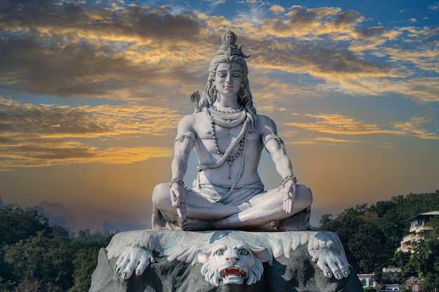 Statue of meditating Hindu god Shiva against the sky and clouds on the Ganges River at Rishikesh village in India, close up