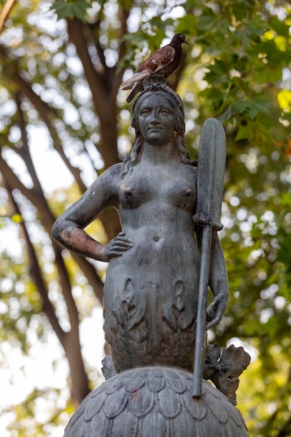 A statue of a mermaid with a sword and pigeon on it