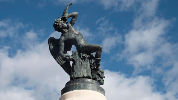 Statue of a person representing the Fallen Angel in black with wings and a snake on a pedestal of gray granite in the Retiro Park in Madrid