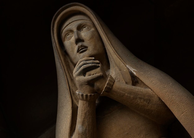 A statue of a woman with a scarf on her head looks up at the sky.