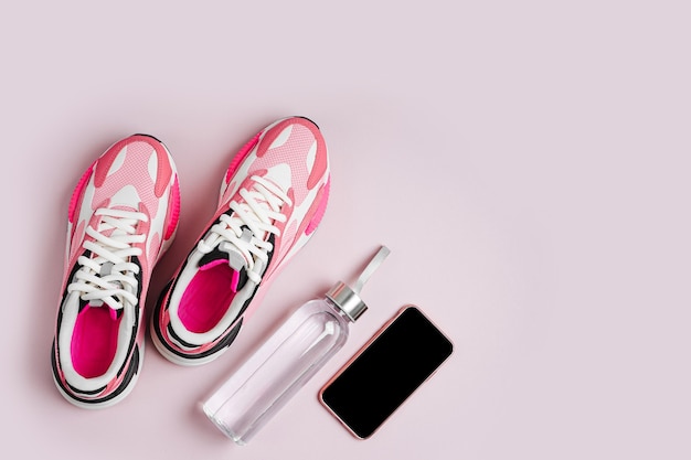 Stay fit. New sneakers and smartphone on a pink background. App for training indoors.