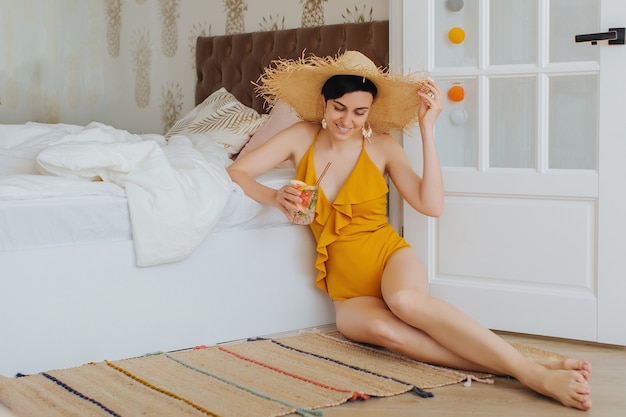 Stay Home, quarantine. Vacation canceled. Young woman in a yellow swimsuit on a bed in a hotel room.