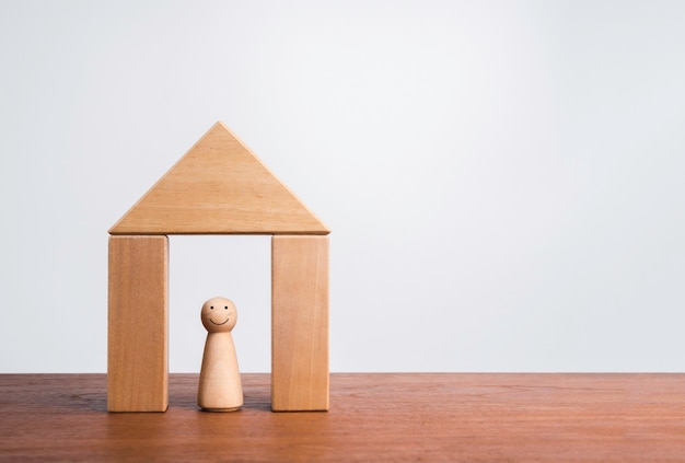 Stay home stay safe, Self-quarantine concept. Home isolation from virus pandemic Covid-19. The wooden figure with happy face stays in the wood house symbol on table, white background with copy space.