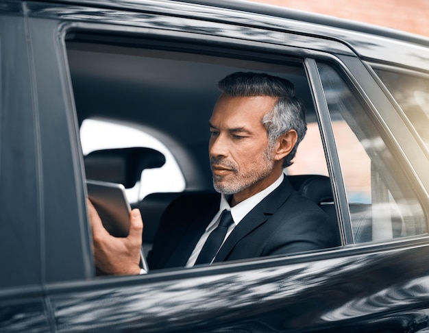 Staying connected is the key to success Cropped shot of a handsome mature businessman using a tablet while sitting in the backseat of a car during his morning commute