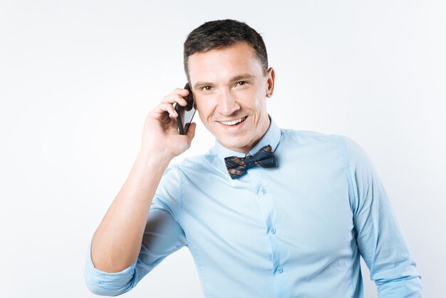 Staying in touch. Delighted positive good looking man putting a phone to his ear and smiling while making a call