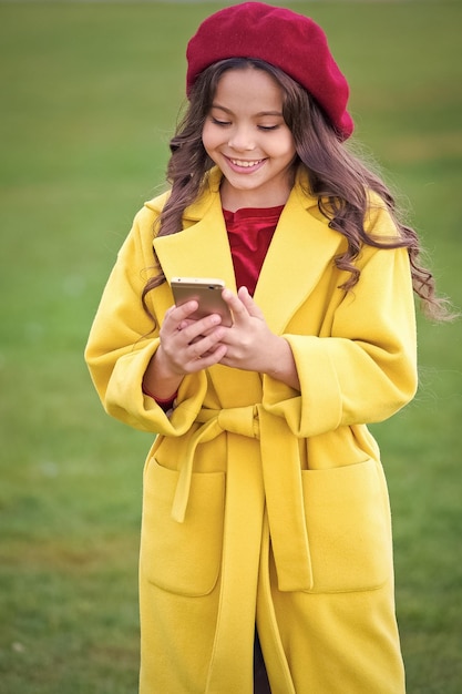 Staying in touch Happy girl read sms in mobile phone Little girl use mobile internet on autumn day Happy childhood and modern life Enjoying autumn time