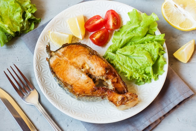 Steak baked salmon fish on a plate with fresh vegetables.