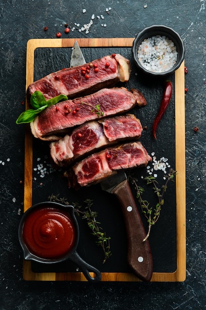 Steak on the bone on the kitchen board Tomahawk steak on a black wooden background Top view Free space for copying