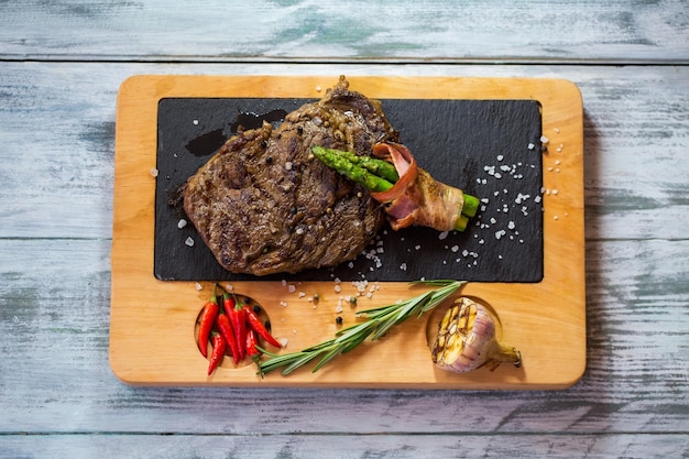 Steak on light brown board. Rosemary and salt. Beef meat cooked by chef. Try out the new dish.