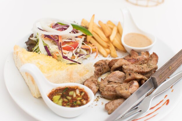 Steak platter with a side dish of bread, salad, sauce, french fries.