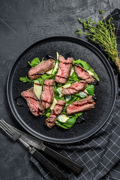 Steak salad with spinach, arugula and sliced beef marbled steak. Black background. Top view.