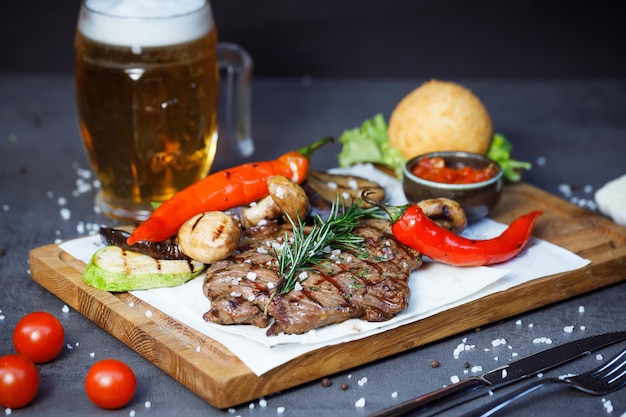 steak with baked vegetables on a plate and a pint of beer in the background