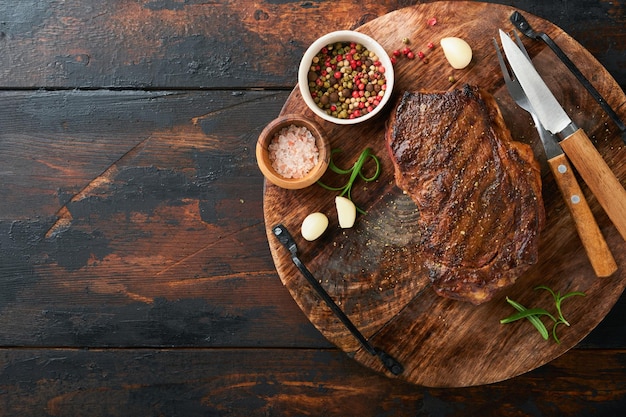 Steaks Grilled New York Steak with spices rosemary and pepper on black marble board on old wooden background Top view Mock up