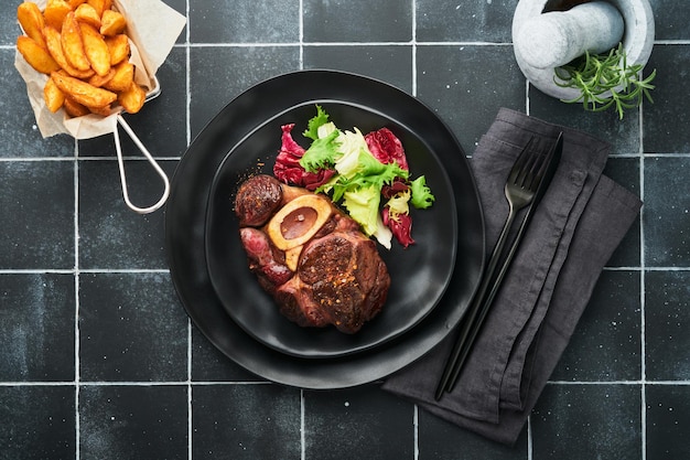 Steaks Osso Buco Sliced beef grilled Osso Buco or porterhouse meat steak with garnished with salad and french fries on black marble board on old wooden background Top view Mock up