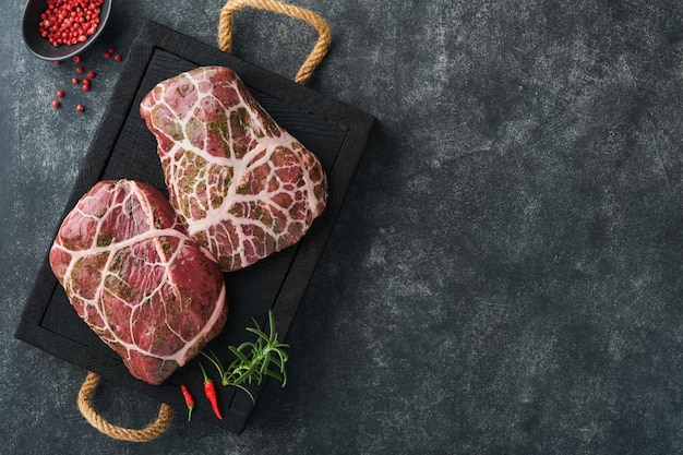 Steaks Raw Raw cowboy steak marbled beef meat with spices rosemary and pepper on black wooden board on old black slate table background Top view Mock up