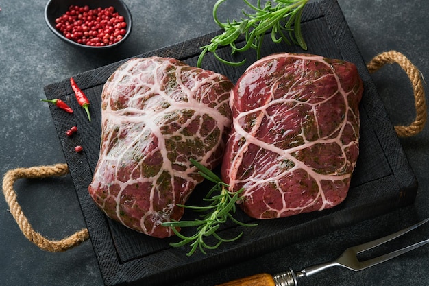 Steaks Raw Raw cowboy steak marbled beef meat with spices rosemary and pepper on black wooden board on old black slate table background Top view Mock up