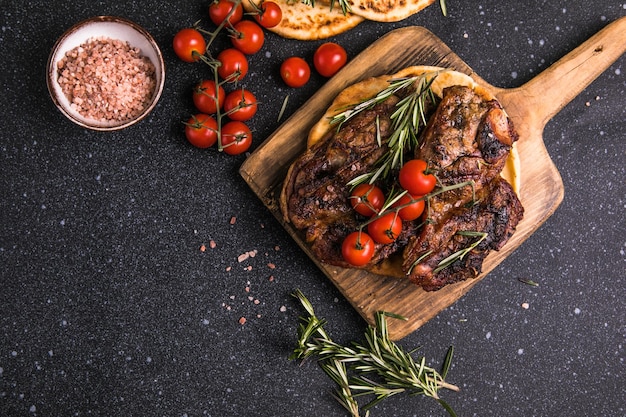 Steaks Sliced grilled meat steak New York or Ribeye with spices rosemary and pepper on black board Top view