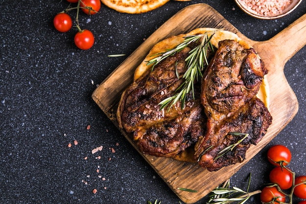 Steaks Sliced grilled meat steak New York or Ribeye with spices rosemary and pepper on black board Top view