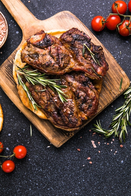 Steaks Sliced grilled meat steak New York or Ribeye with spices rosemary and pepper on black board Top view