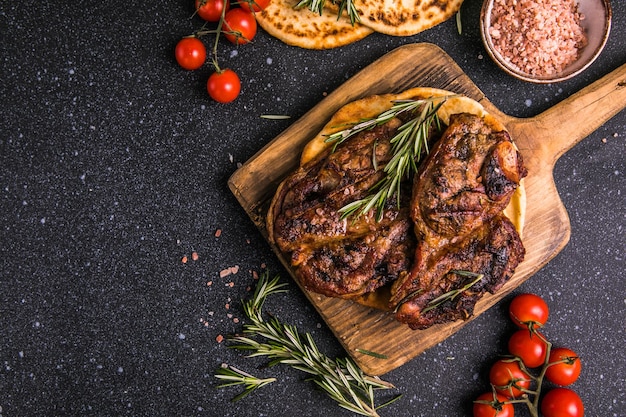 Steaks Sliced grilled meat steak New York or Ribeye with spices rosemary and pepper on black board Top view