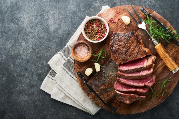 Steaks Sliced grilled meat steak New York or Striploin with spices rosemary and pepper on black marble board on old stone grey background Top view Mock up