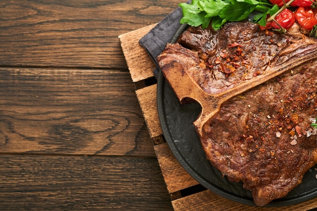 Steaks Tbone Sliced beef grilled Tbone or porterhouse meat steak with spices rosemary and pepper on black marble board on old wooden background Top view Mock up