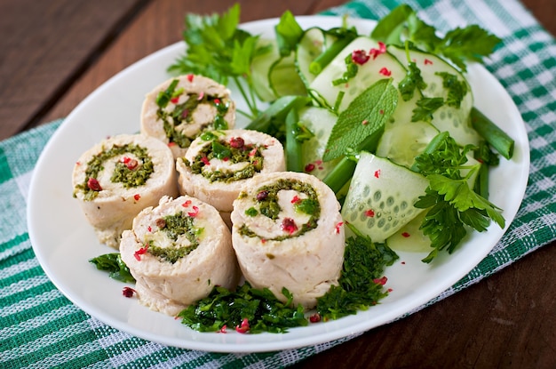 Steamed chicken rolls with greens and fresh vegetable salad on a brown plate