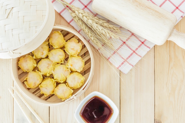 Steamed dumplings (chinese dim sum) in bamboo basket, serve with chopsticks on wooden tabl