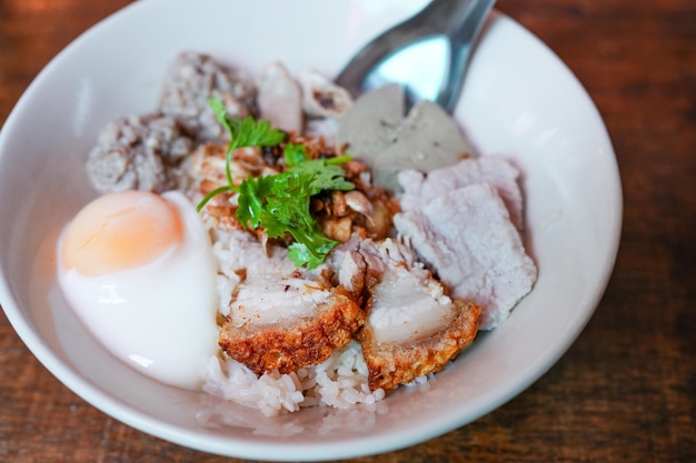 Steamed rice topping with boiled egg crispy pork and coriander on wooden table