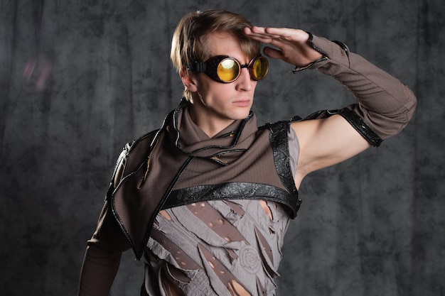 Steampunk or post-apocalyptic style character, a young man in a grunge suit. A jacket with fastened sleeves with slits m goggle flight glasses on his head, a grunge outfit