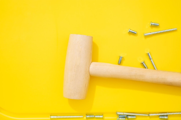 Steel screws and wooden mullet for furniture different types on yellow background Top view