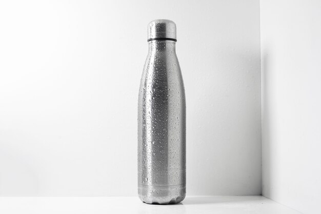 Steel thermo bottle sprayed with water on white.