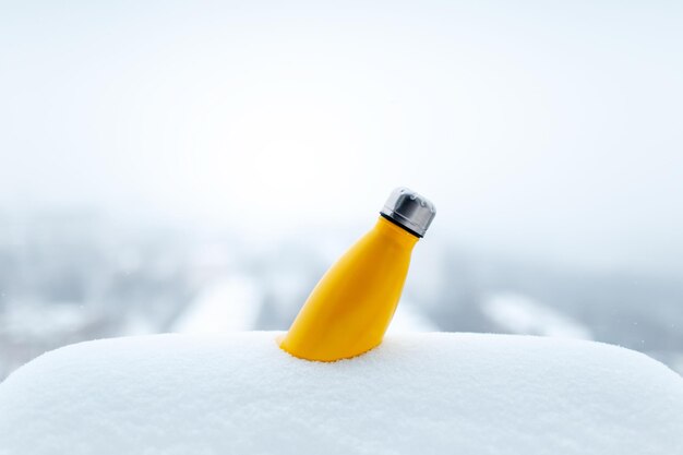 Steel thermo bottle of yellow color in snow Closeup view Reusable thermos