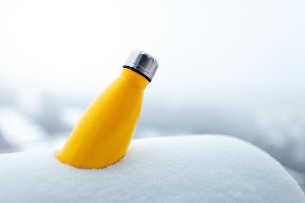 Steel thermo bottle of yellow color in snow Closeup view Reusable thermos