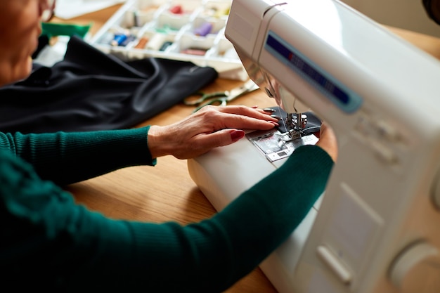 Step by step, 50-yers old woman sews clothes on sewing machine, Mature tailor working with sewing in atelier, textile industry, hobby, workspace. Creation process DIY, Workplace of seamstress.