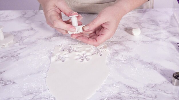 Step by step. Cutting out snowflakes with cookie cutters out of white fondant on a marble counter.