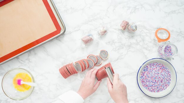 Step by step. Flat lay. Slicing dough with a dough knife to bake red, white, and blue pinwheel sugar cookies.