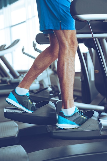 Step by step to get fit. Side view part of young man in sports shoes working out on stepper at gym