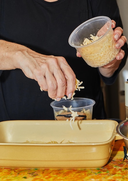 Step by step potato gratin recipe Hands toss grated cheese onto potato slices in glass baking dish Potato casserole