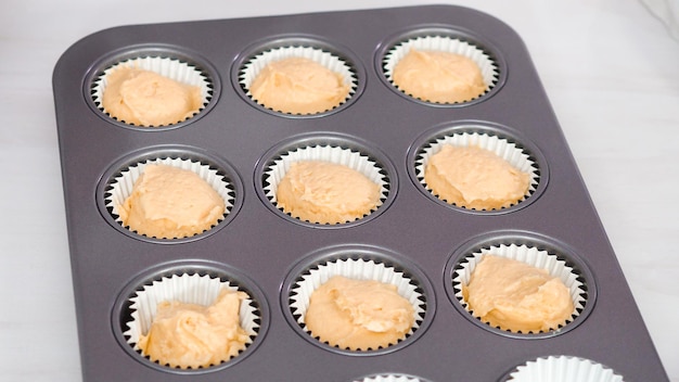 Step by step. Scooping cupcake batter into cupcake liners to bake vanilla cupcakes.