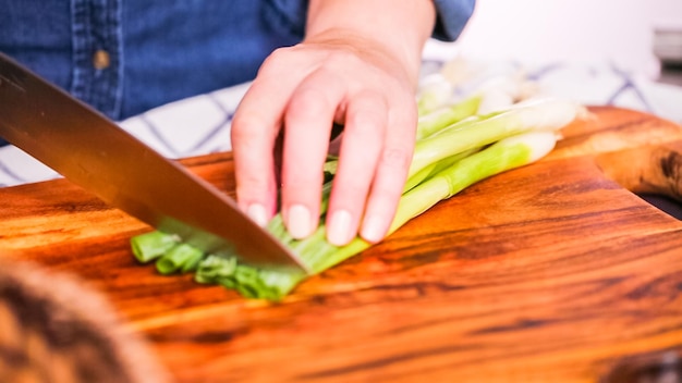 Step by step. Slicing green onions on a wood cutting board.