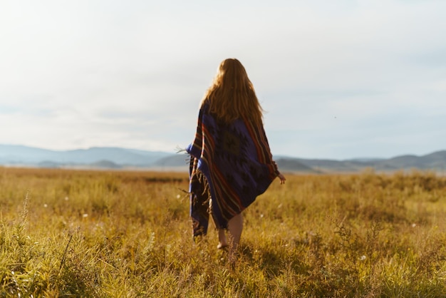 On the steppe grass in the distance towards the hills goes barefoot girl in a long cape with long re