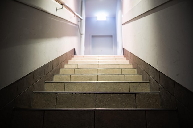 Steps leading up and a light at the end of the corridor with a glowing exit sign A corridor with steps illuminated by lamps