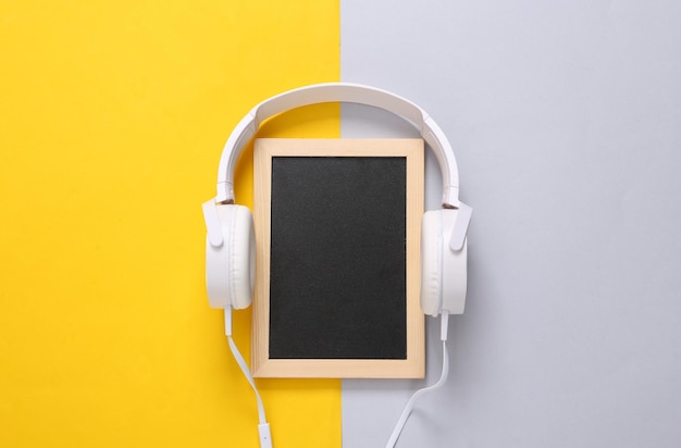 Stereo headphones and blank mini chalk board for copy space on gray yellow background